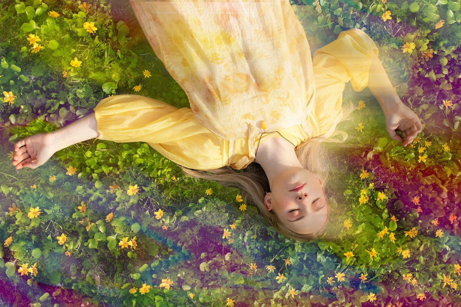 A young woman in a yellow dress lies peacefully among colorful wildflowers in a lush green meadow.