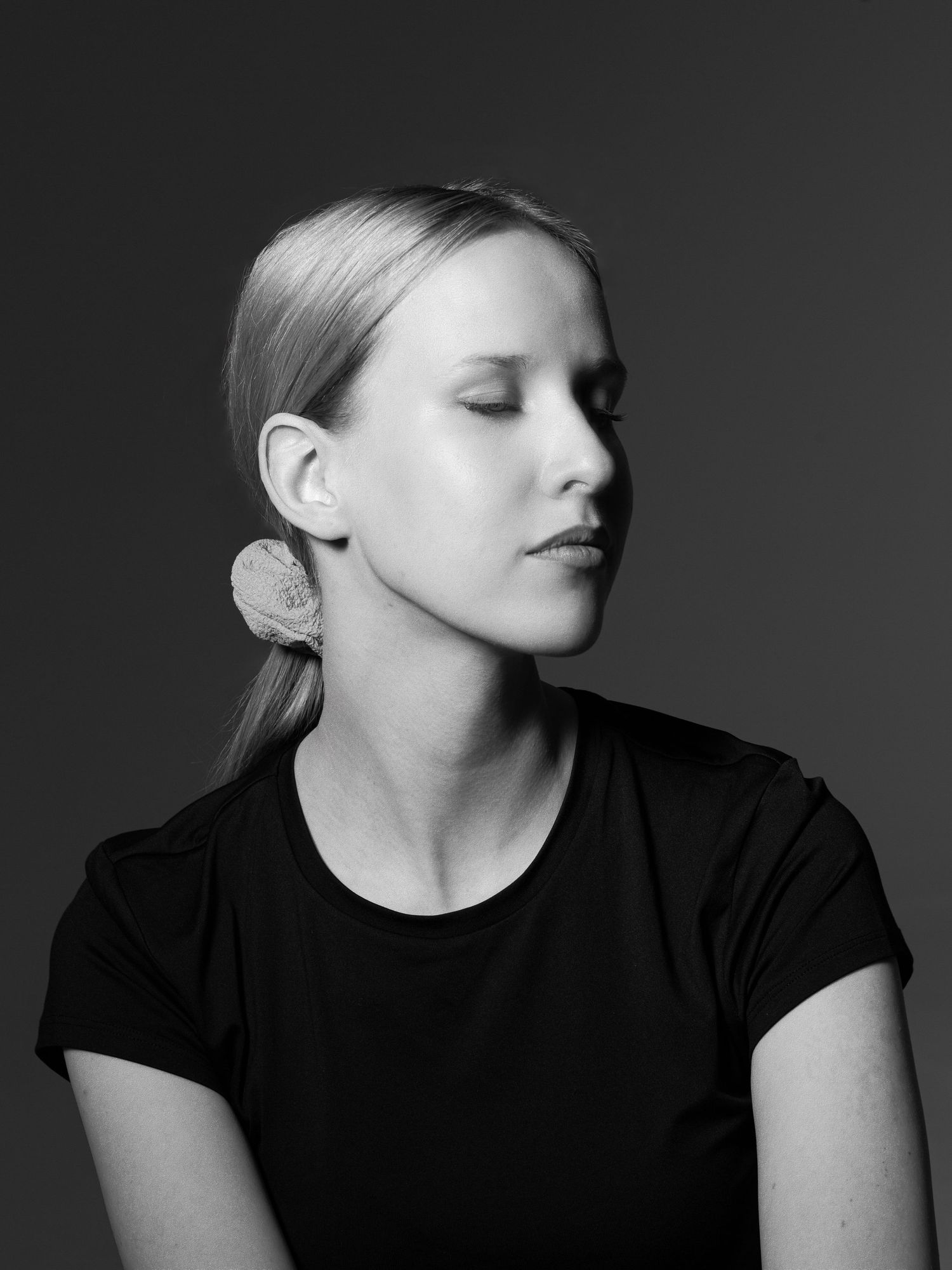 Black and white side profile of blonde woman in black t-shirt wearing a large statement earring.