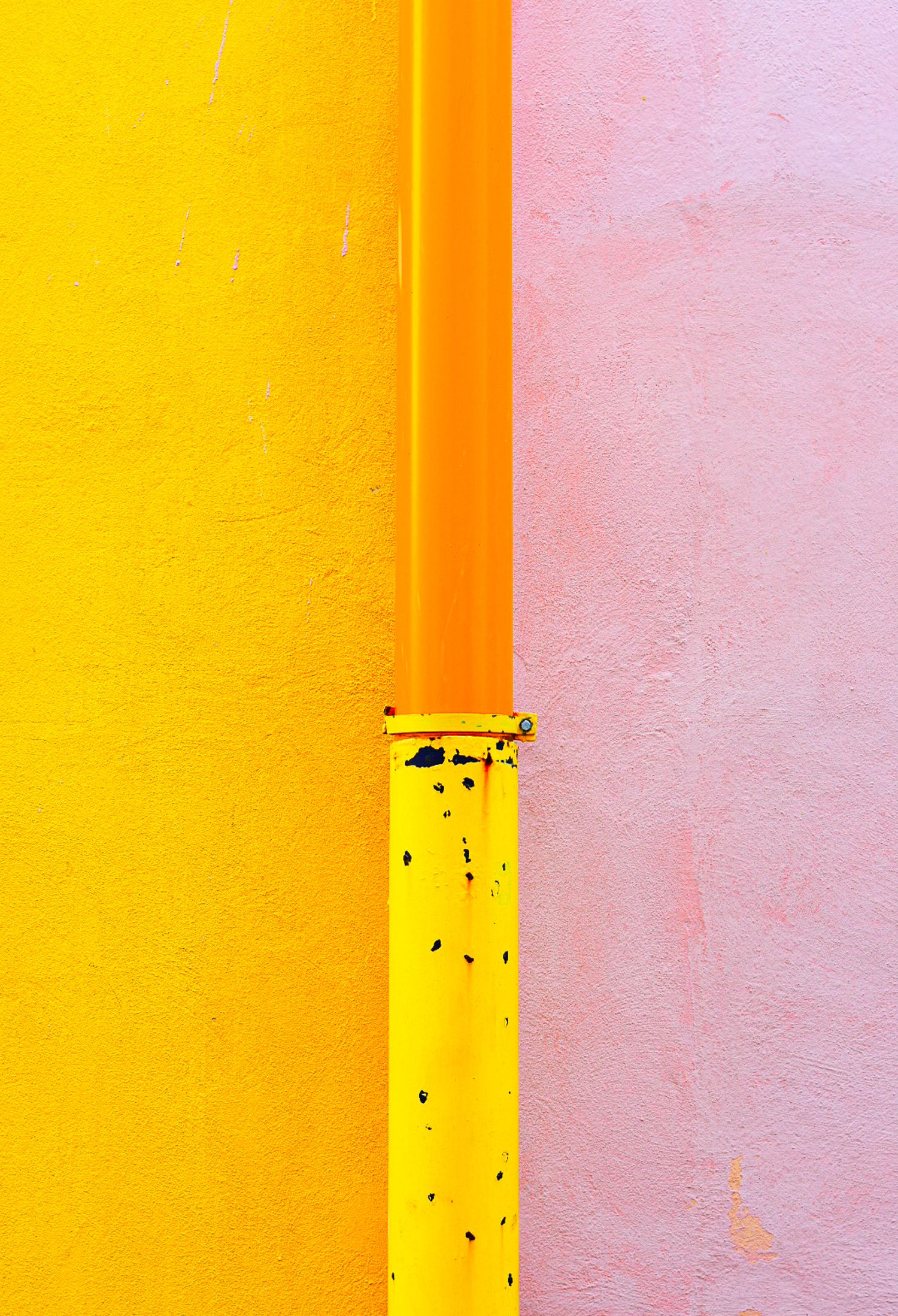 Yellow pipe against vibrant yellow and pink painted walls, minimalist urban abstract photography.