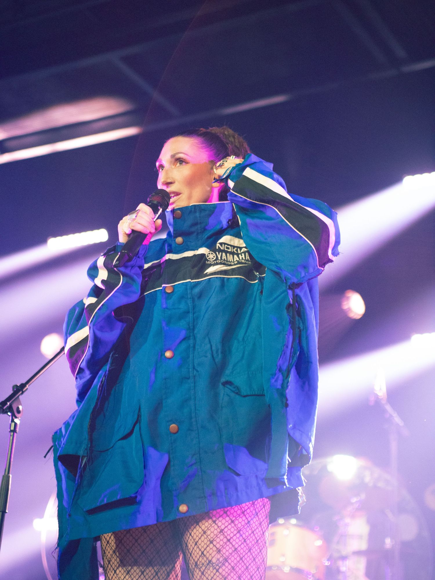 Female singer performing on stage wearing a blue Yamaha jacket and fishnet stockings.