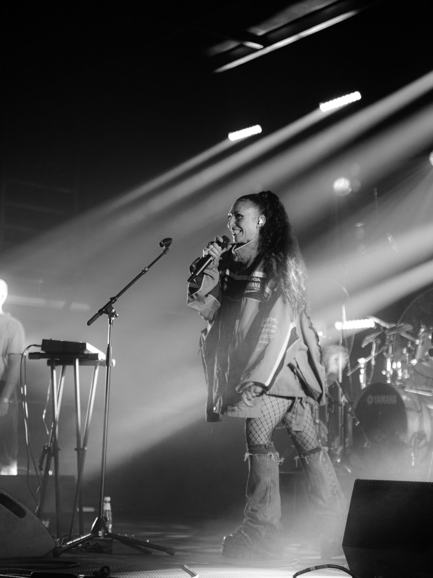 Black and white concert photo of a female vocalist singing passionately under stage spotlights.