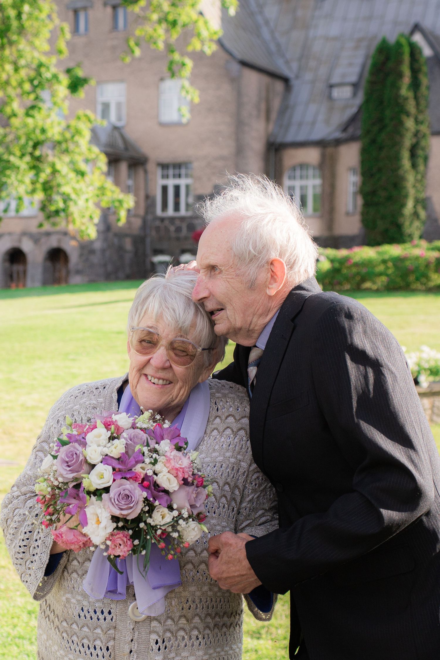 Happy elderly couple sharing a joyful moment outdoors, woman holding a purple and white bouquet.