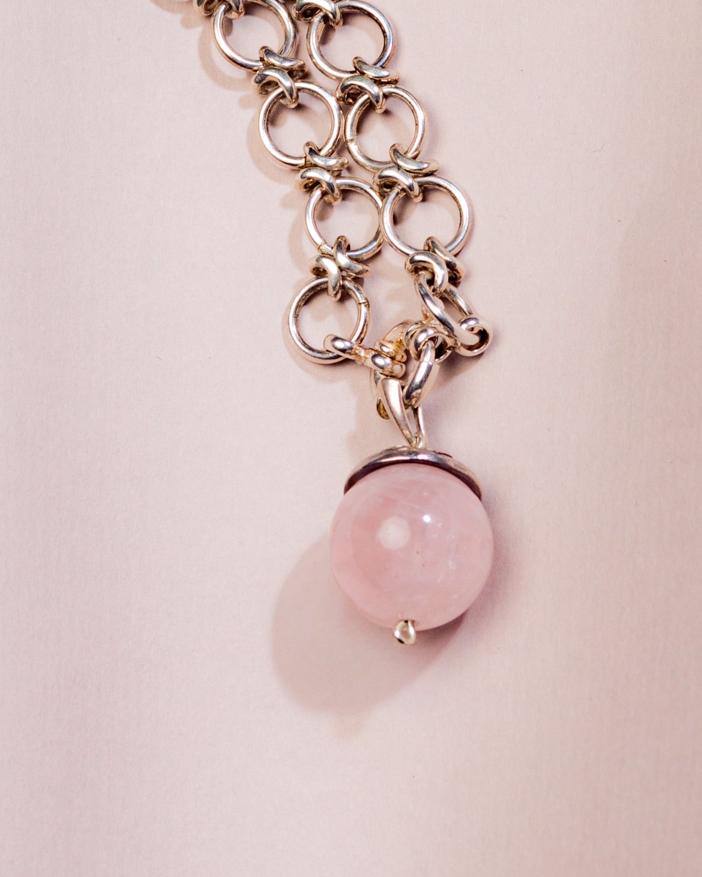 Silver chain bracelet with a pink rose quartz ball pendant charm on a light pink background.