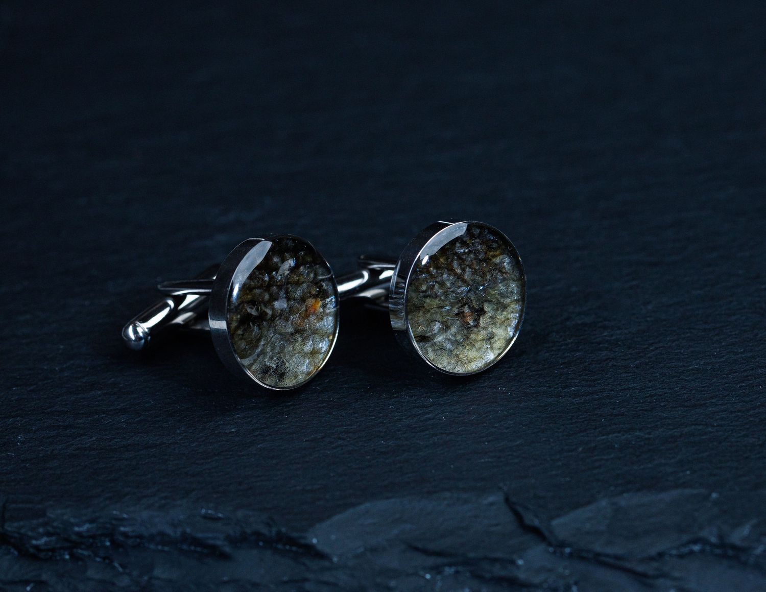 Elegant oval silver cufflinks with natural stone inlay on dark slate background.