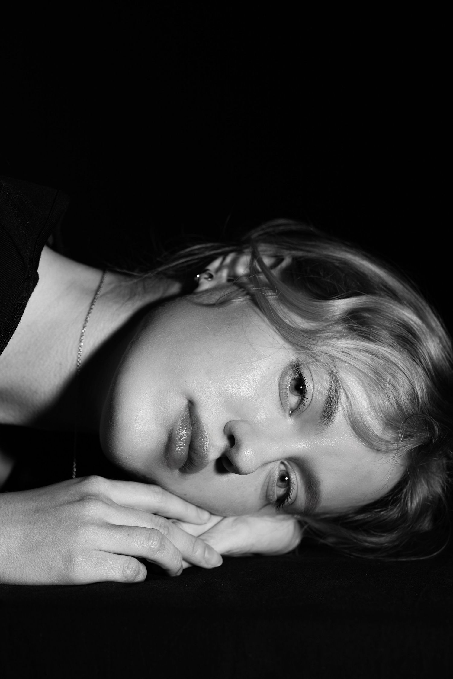 Black and white portrait of a young woman resting her chin on her hands against a dark background.