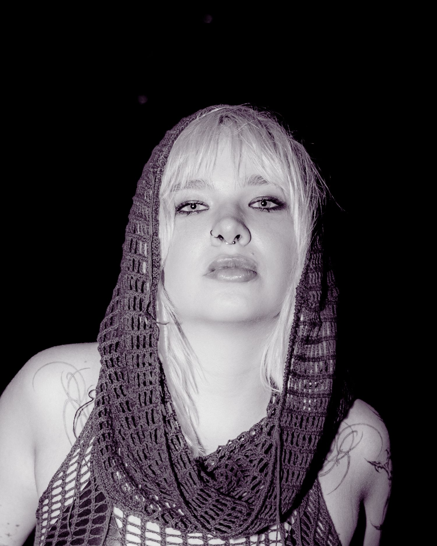 Black and white portrait of a blonde woman wearing a crochet mesh hood.