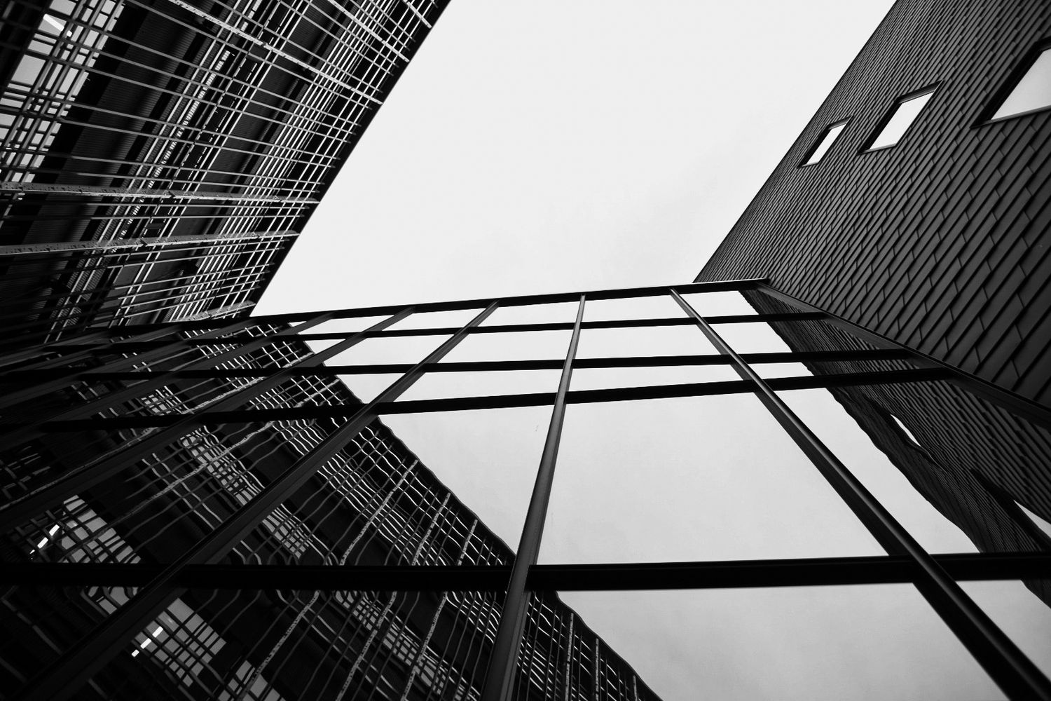 Low angle black and white view of modern glass and steel skyscrapers reaching toward an overcast sky.