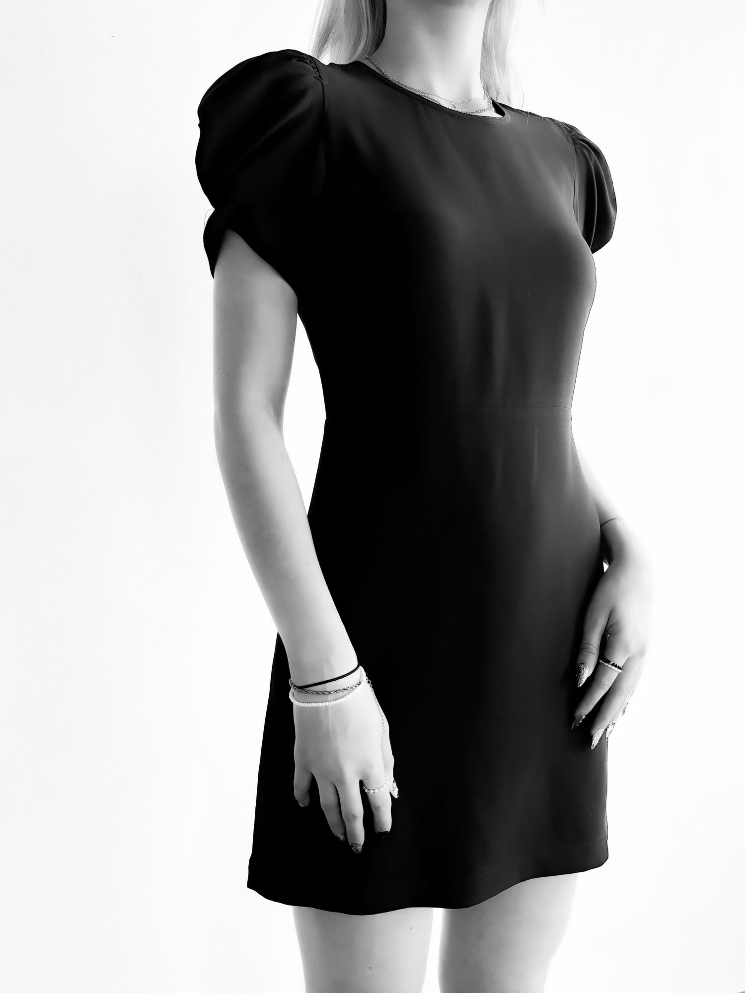 Woman wearing a classic black mini dress with puff sleeves, styled with silver bracelets and rings, in black and white.
