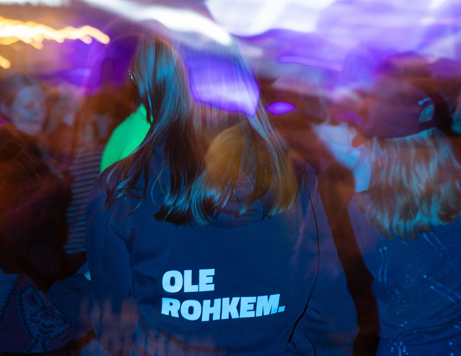 Person wearing a blue jacket reading Ole Rohkem dancing at a concert event.