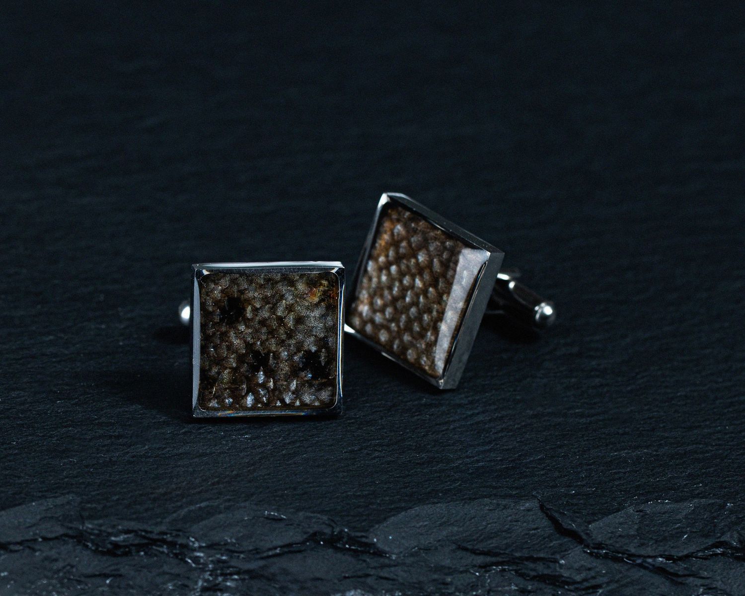 Square silver cufflinks with brown textured fish scale inlay on dark slate background.