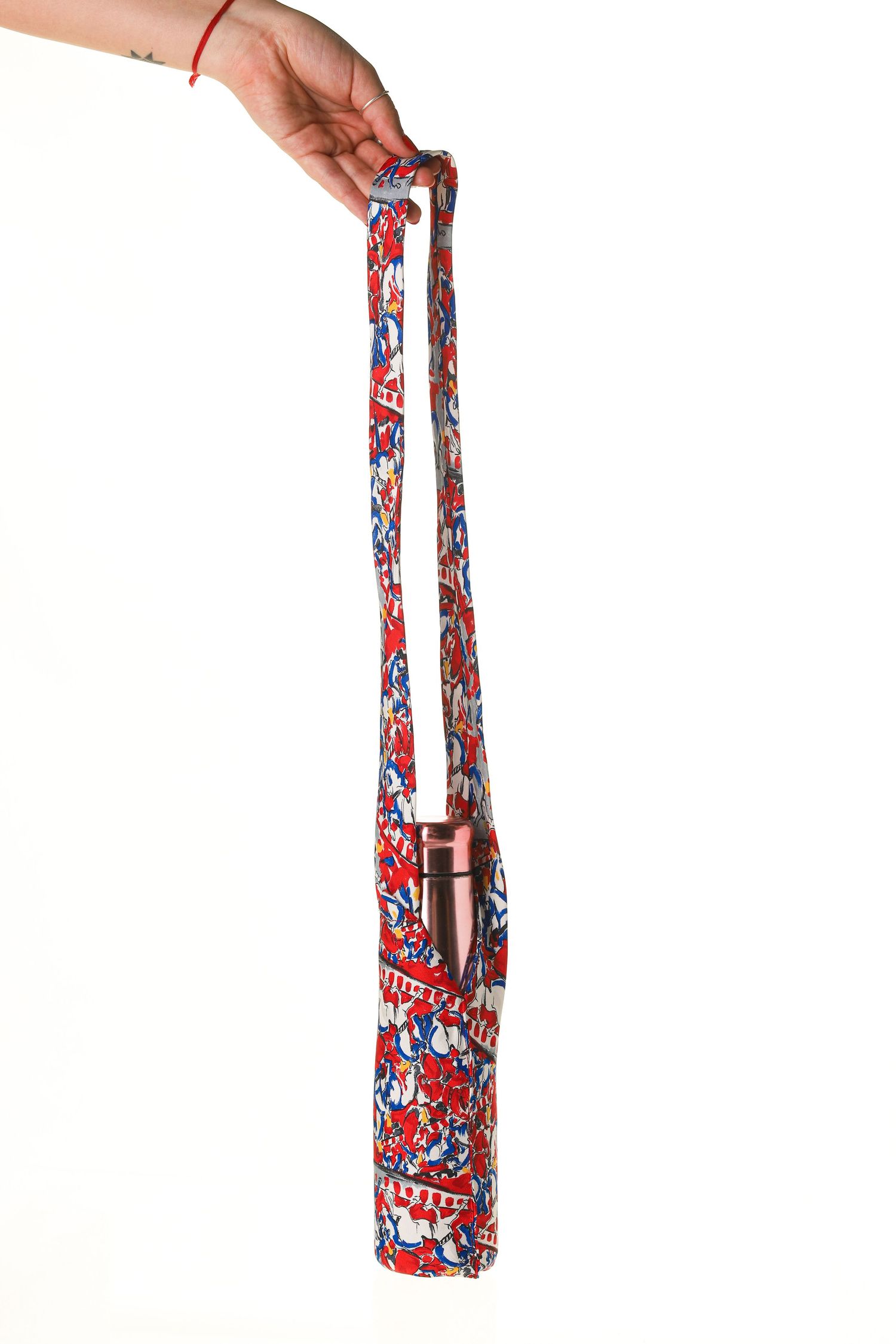Hand holding a colorful red floral patterned yoga mat bag with copper water bottle holder on white background.