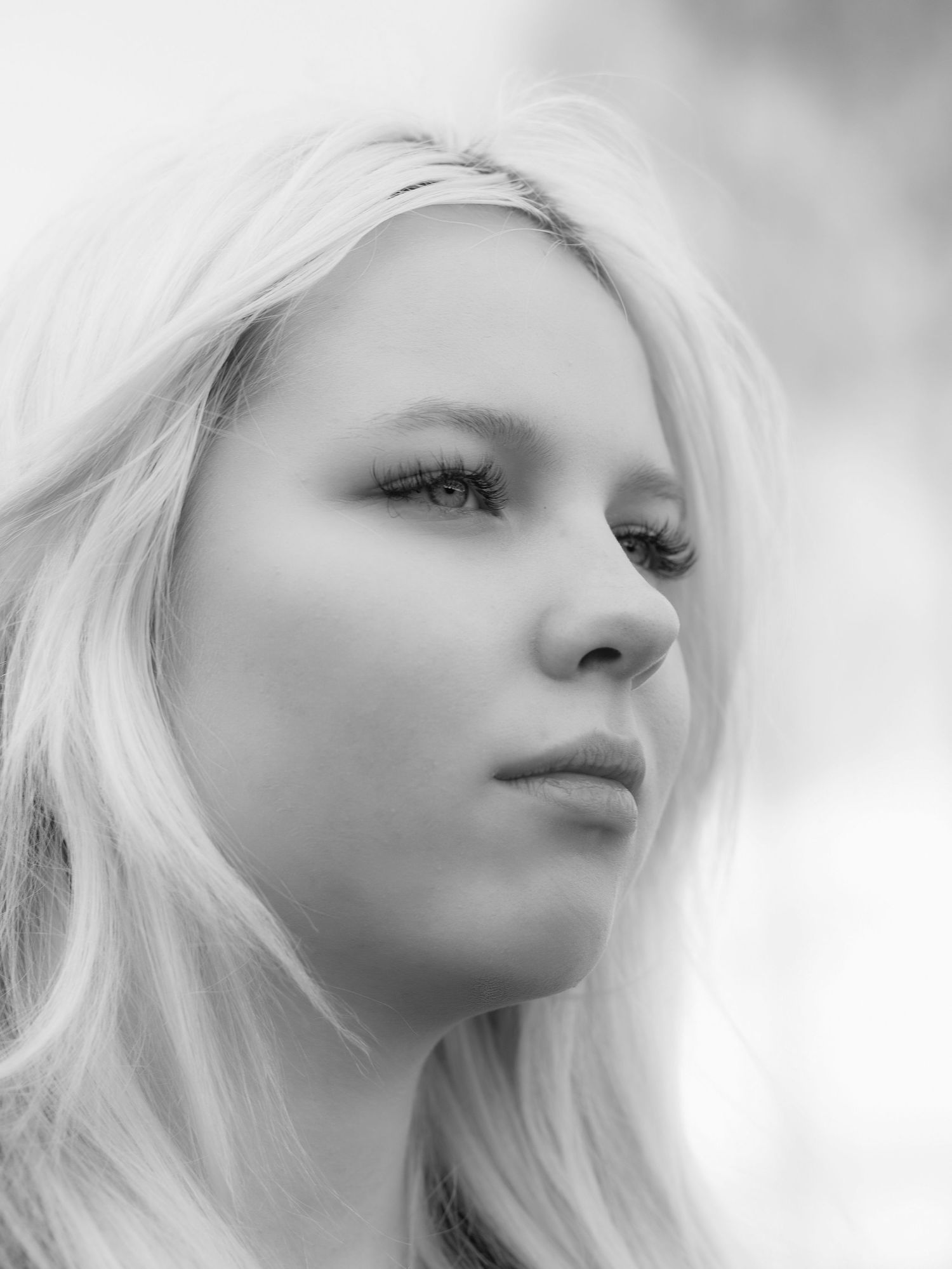 Black and white portrait of a young blonde woman with long hair gazing thoughtfully into the distance.