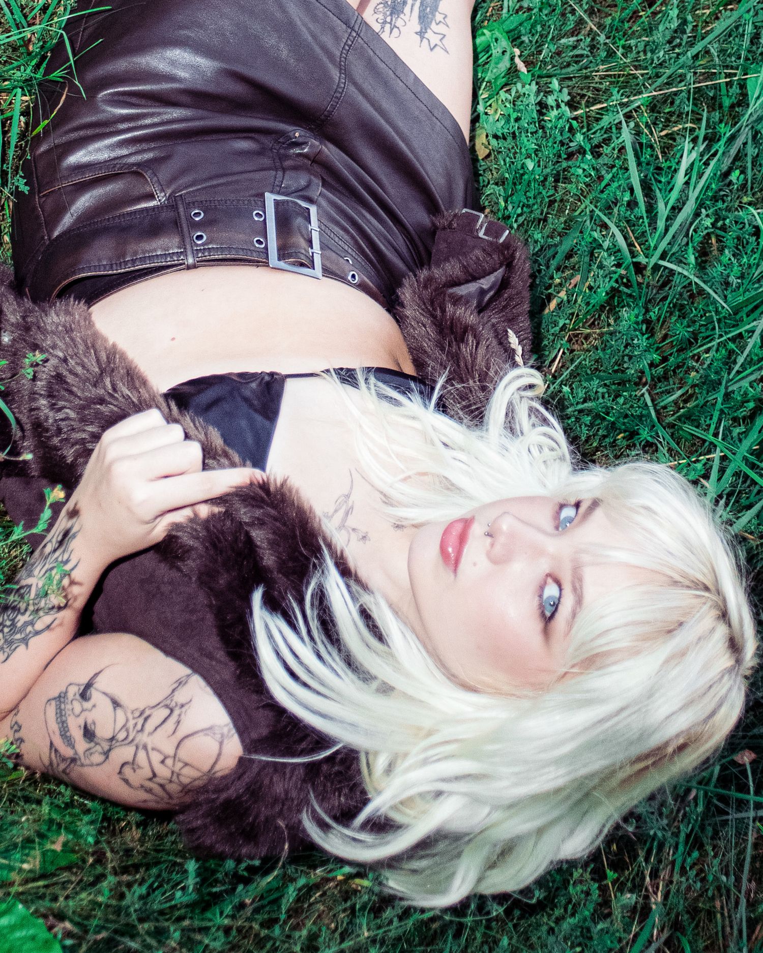 Tattooed blonde woman lying on grass in leather outfit.