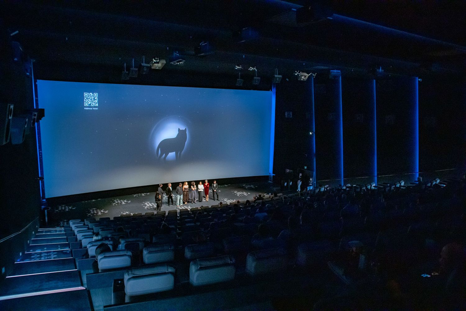 Wide shot of a cinema audience watching a film festival premiere with wolf logo on screen.