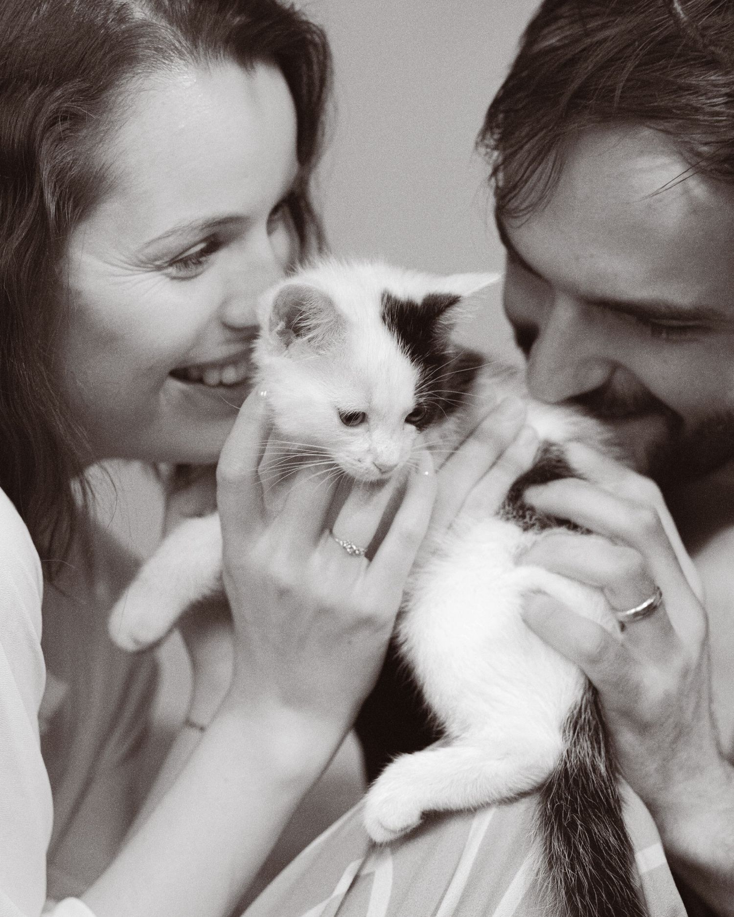 Black and white photo of a smiling couple holding and admiring an adorable black and white kitten together.