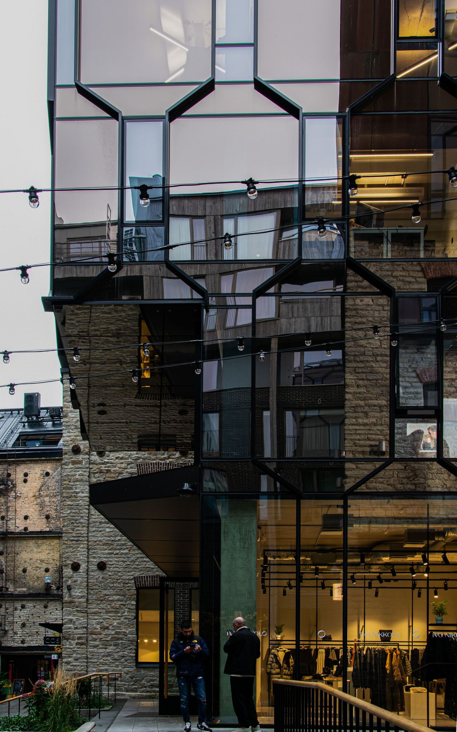 Modern building exterior featuring glass facade, steel framework, and stone walls with illuminated retail space below.