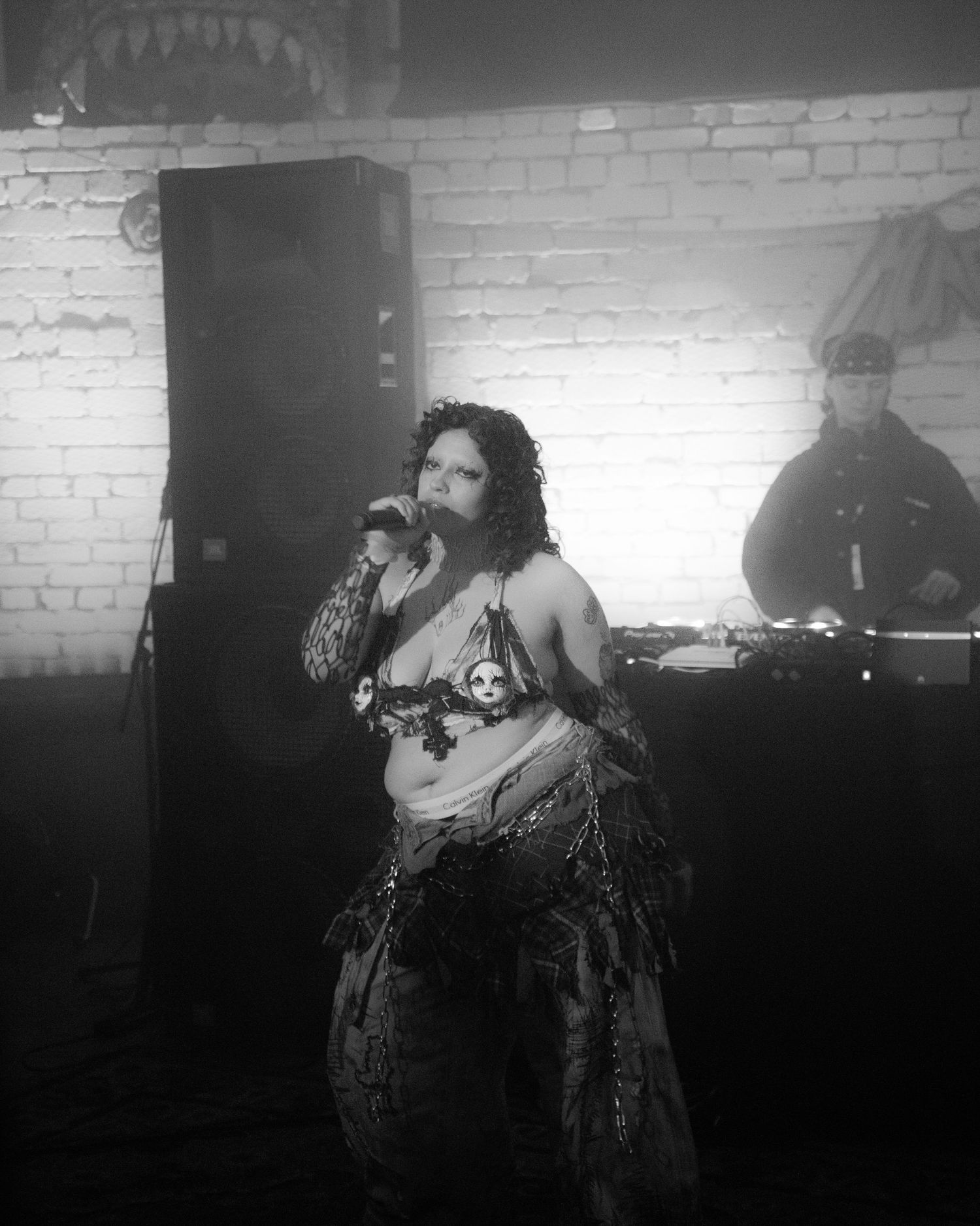 Black and white photo of a performer singing in elaborate costume at a small venue.