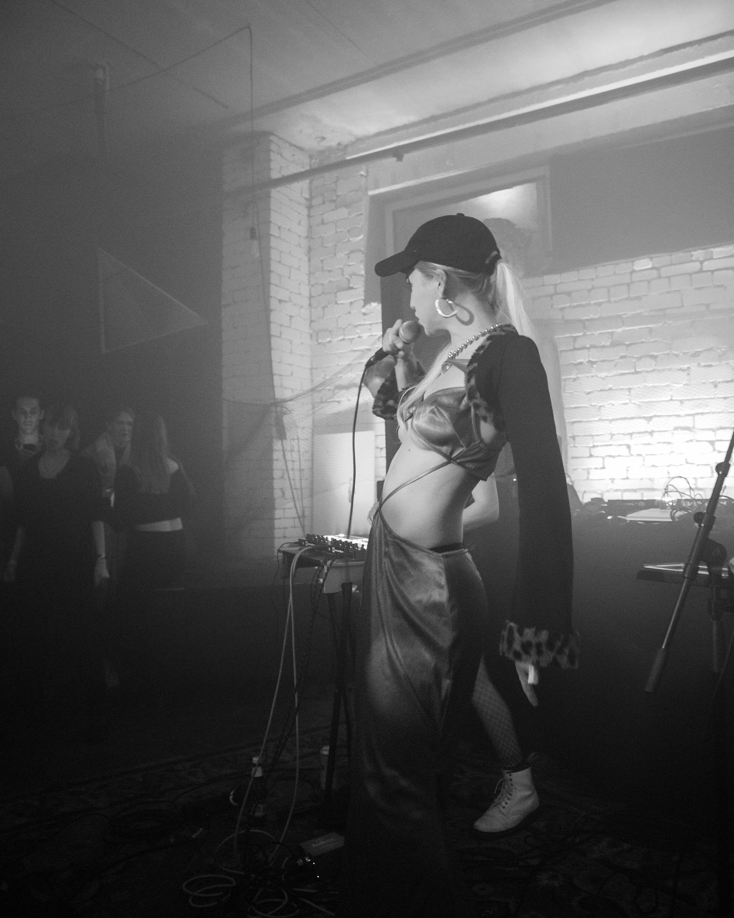 Black and white photo of a female vocalist singing into a microphone in a smoky intimate venue.