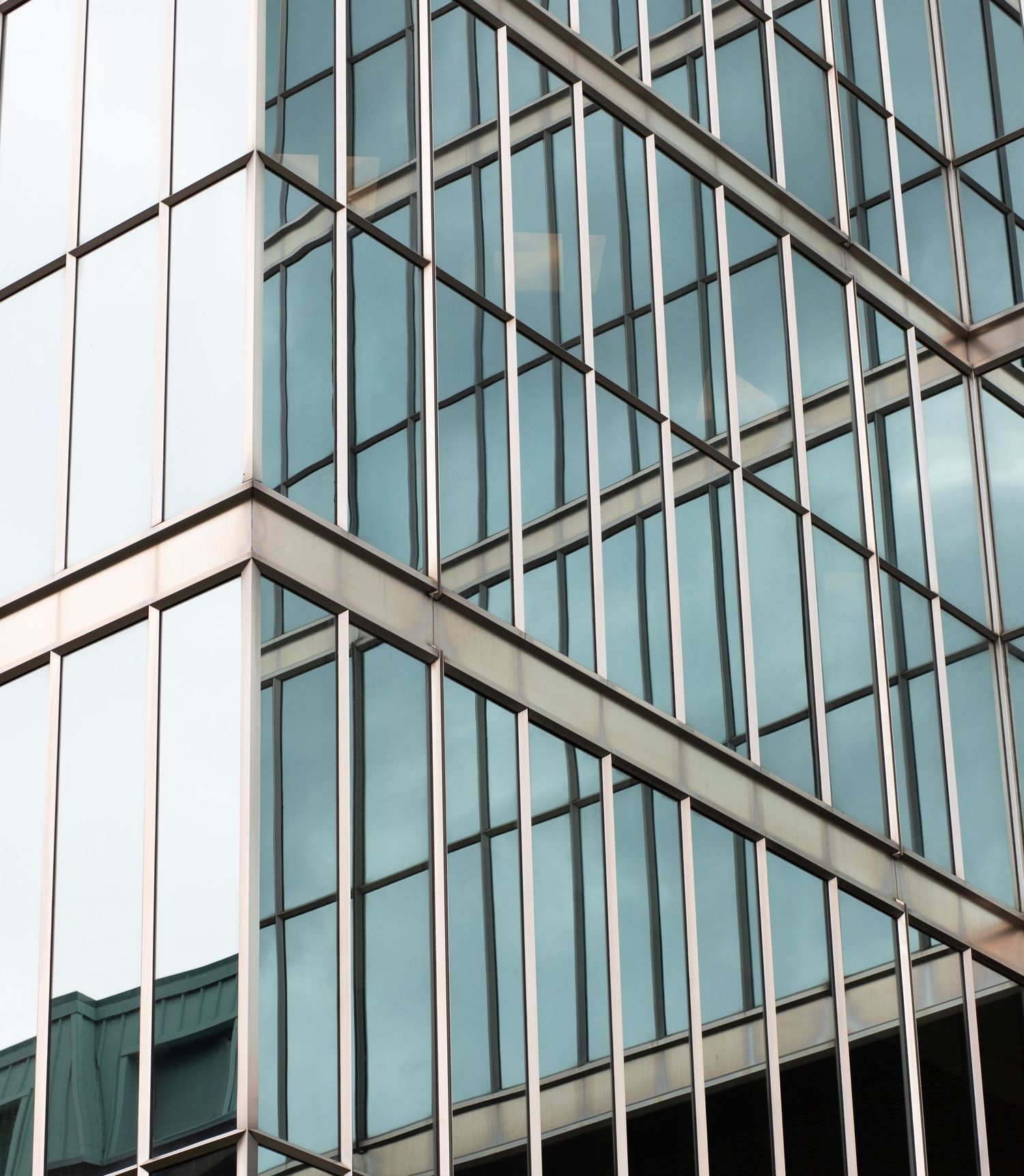 Modern glass curtain wall building facade with blue reflective windows and steel grid framework.