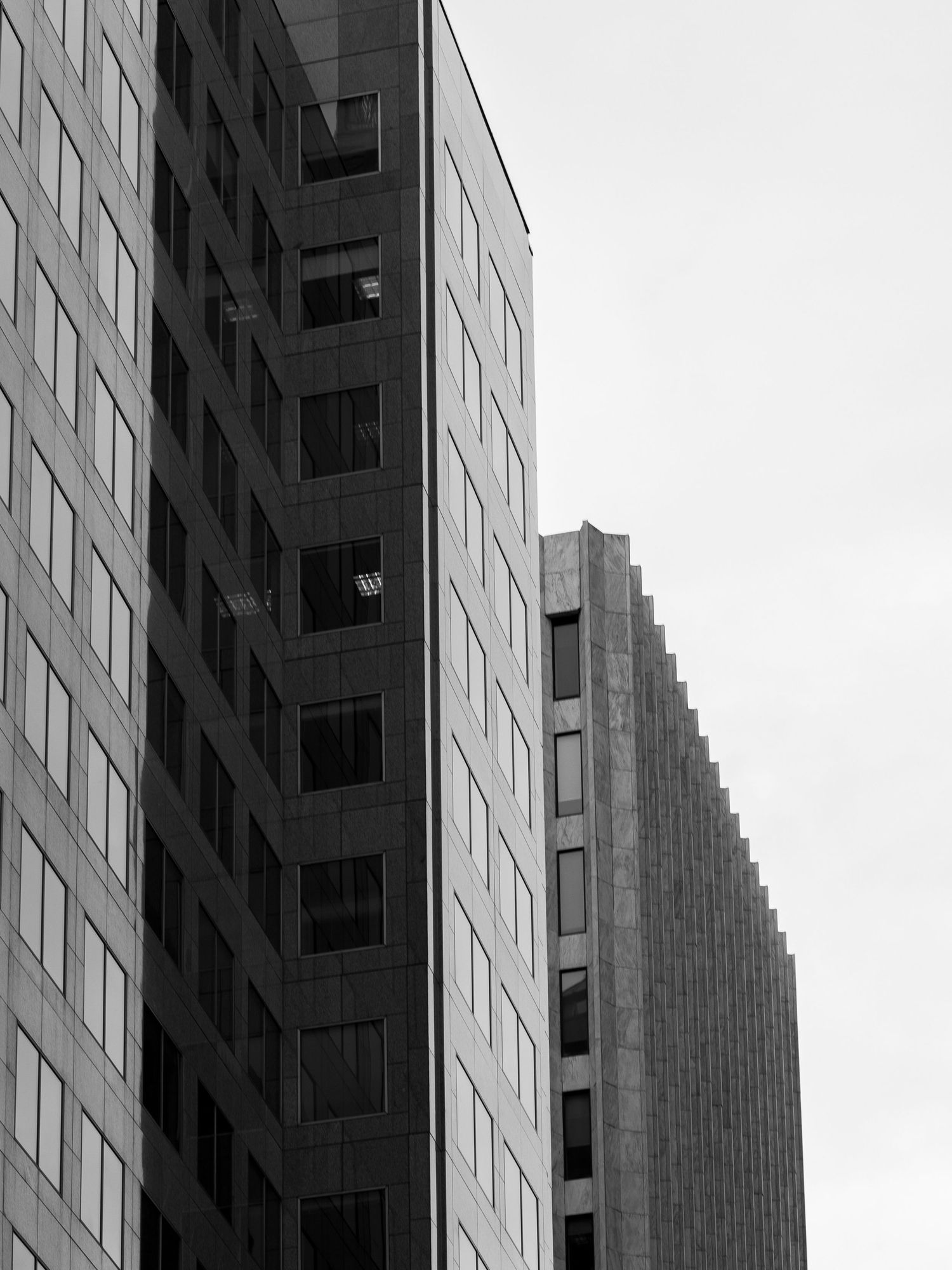 Black and white photo of two modern skyscrapers with grid windows against a pale sky.