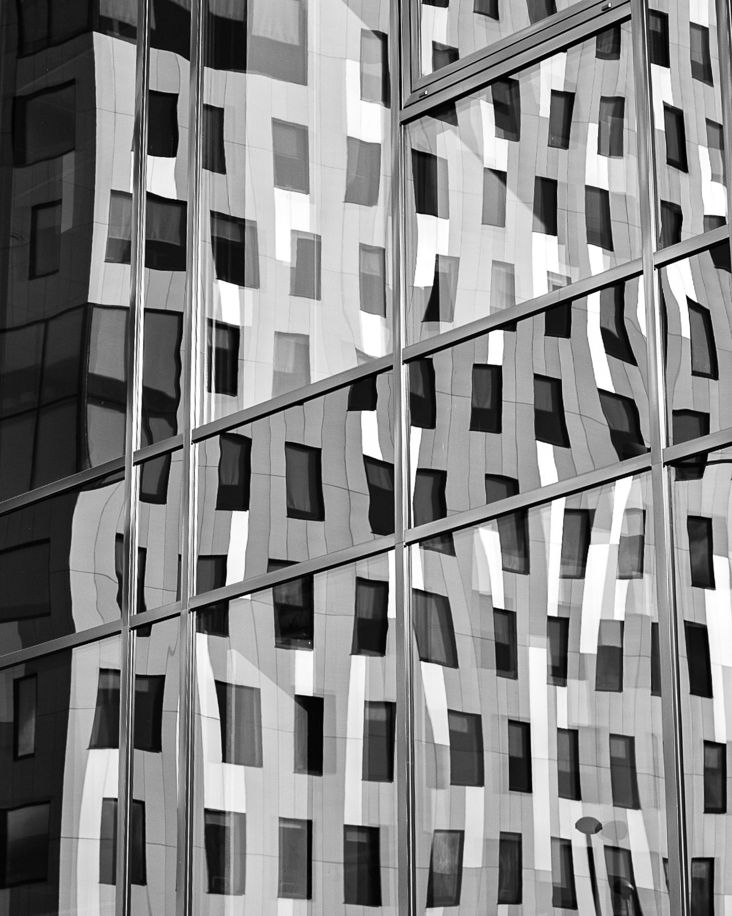 Black and white photo of a modern glass building facade with geometric patterns and reflections.