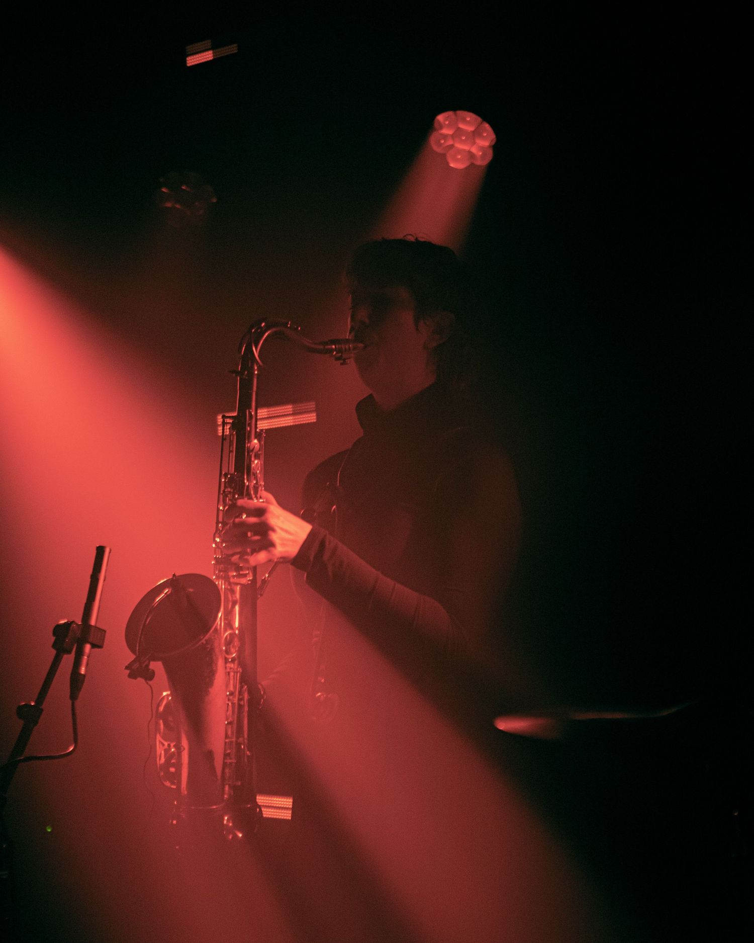 Musician playing saxophone on stage under dramatic red and white spotlights in a dark concert venue.