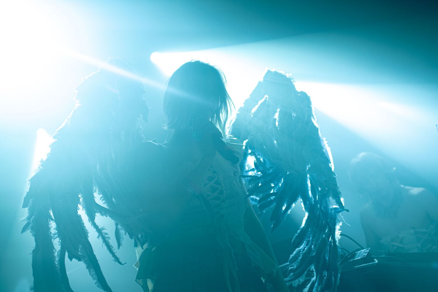 Two performers in tattered costumes on stage bathed in dramatic teal stage lighting during a live concert.