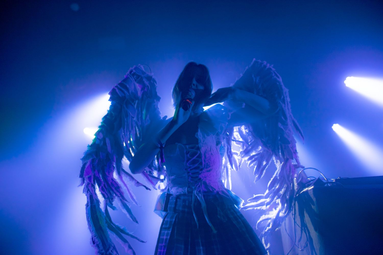 Performer in dramatic angel wings costume under blue stage lighting at a live concert event.