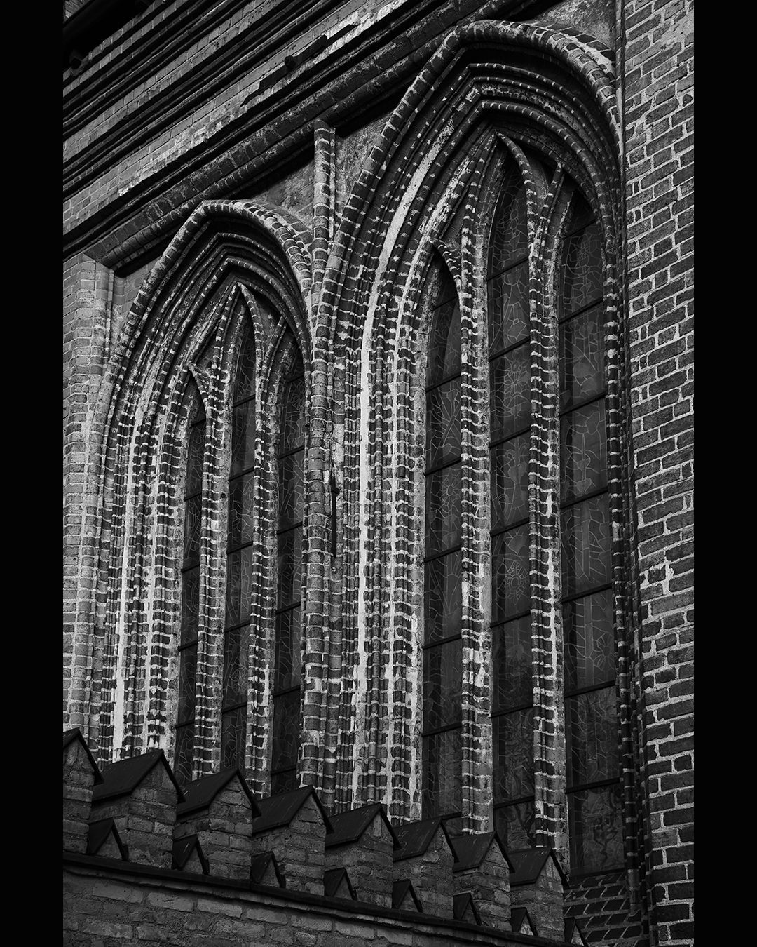 Black and white close-up of Gothic brick cathedral windows with ornate arched stonework.