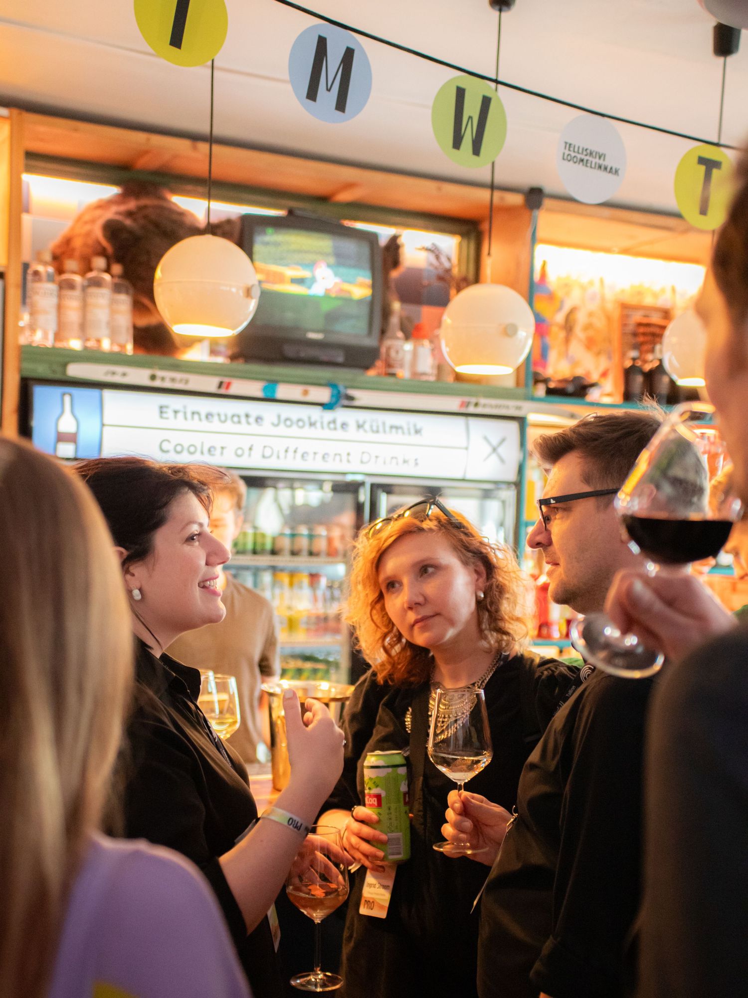 People socializing and drinking wine at a colorful bar event with festive decorations.