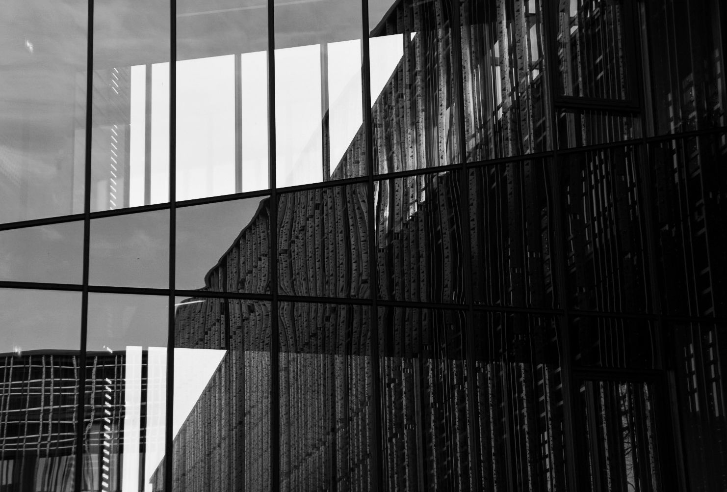 Black and white photo of modern glass building facade reflecting urban architecture and city skyline.