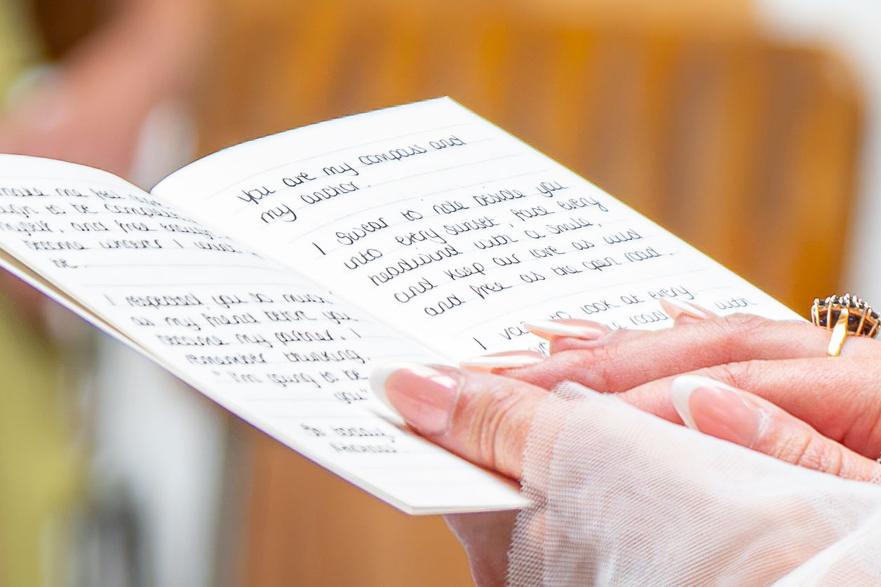 Person holding open a handwritten booklet with cursive wedding vows written on white pages.