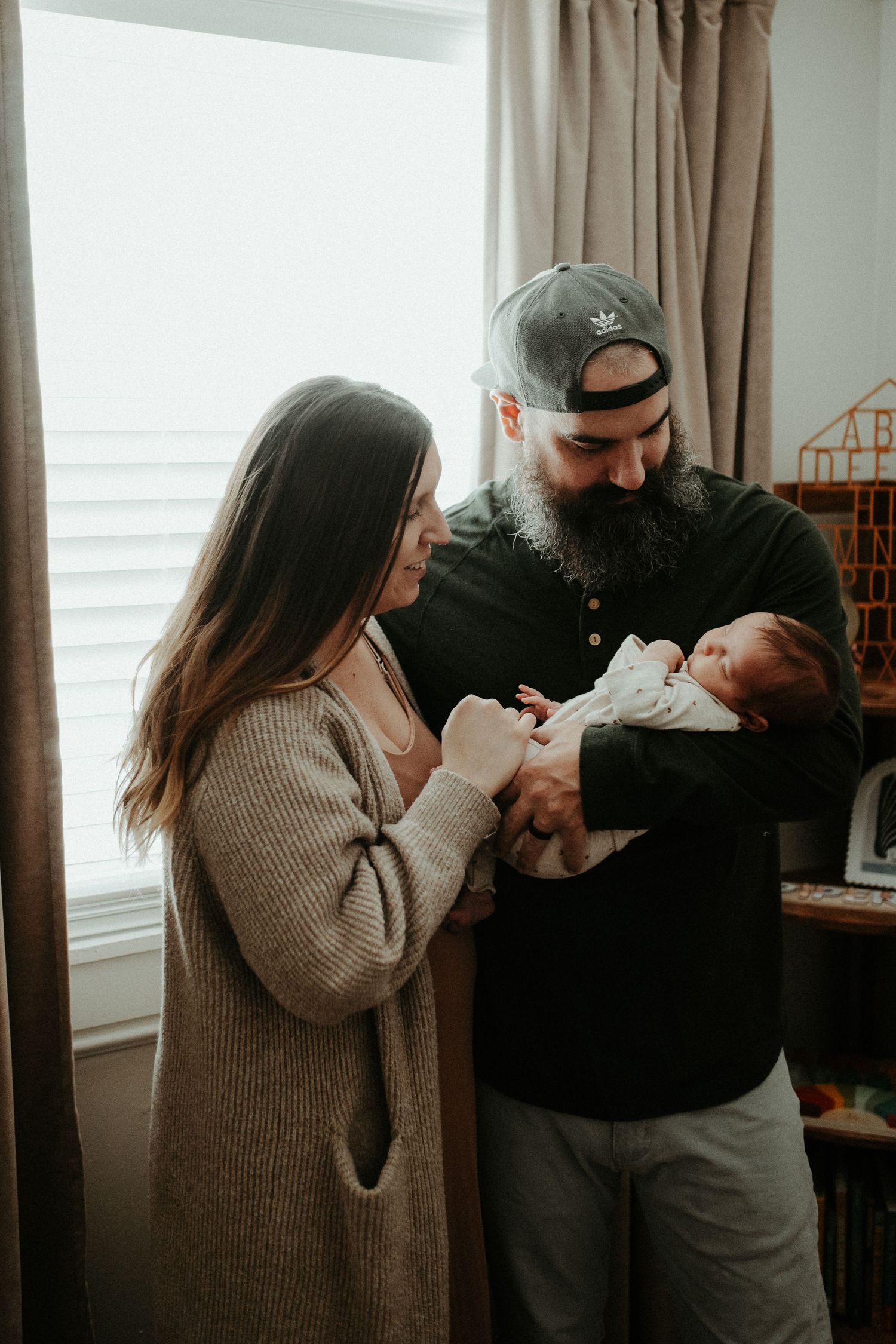 Parents sharing a tender moment while holding their newborn baby in a cozy home setting.