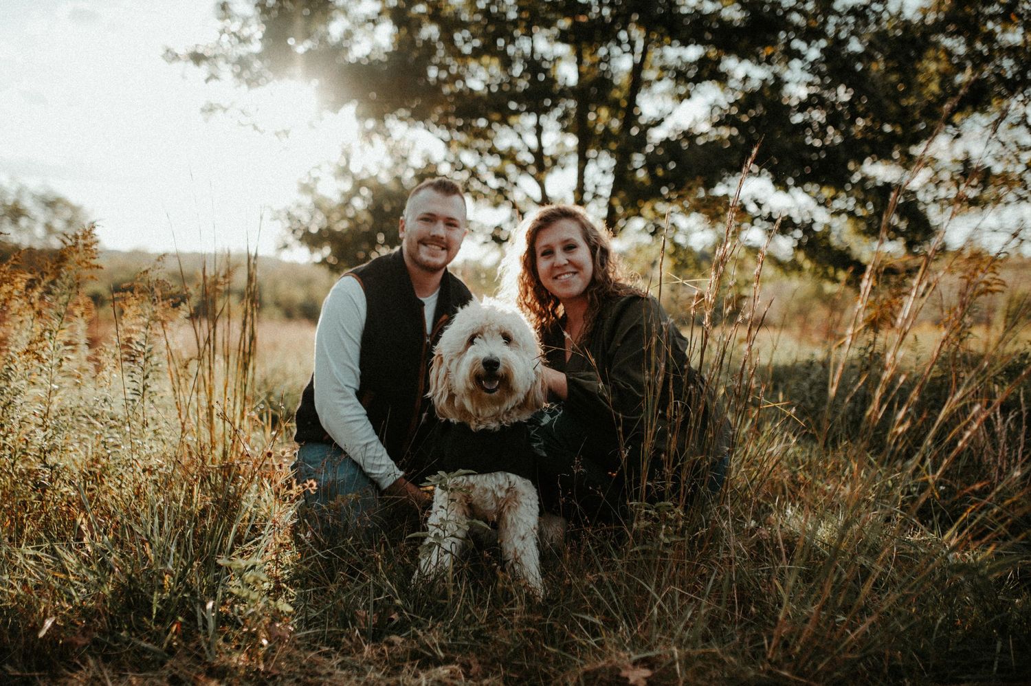 Couple poses with their fluffy white dog in a golden autumn field at sunset. Pittsburgh Wedding Photographer