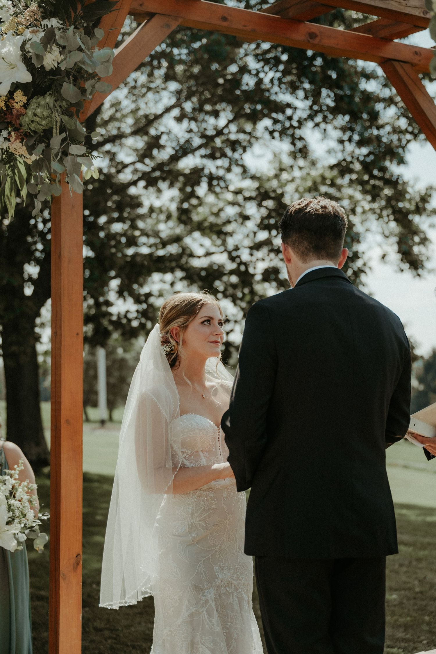 A bride and groom stand beneath a wooden wedding arch during their outdoor ceremony. Pittsburgh Wedding Photographer