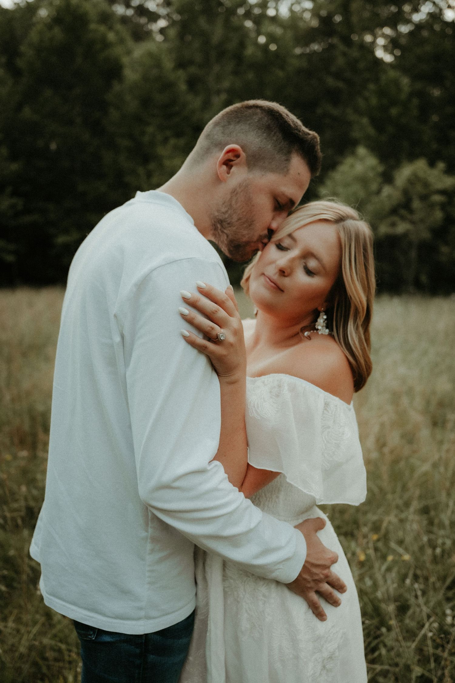 A couple shares intimate moments in a field setting wearing white clothing as they embrace and kiss. Pittsburgh Wedding Photographer