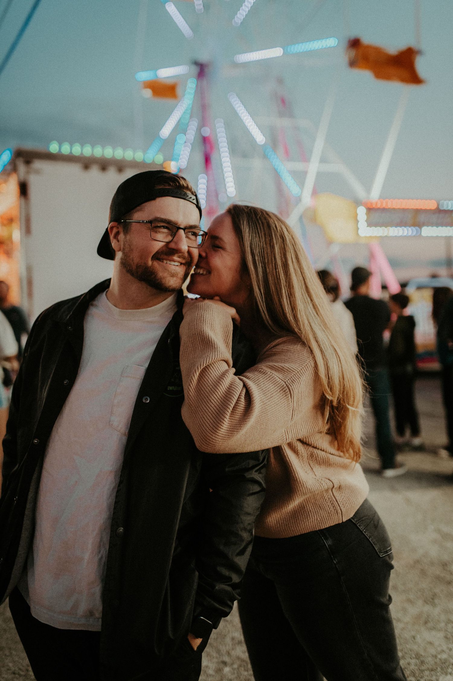 A romantic moment at a carnival with colorful lights and rides in the background. Pittsburgh Wedding Photographer