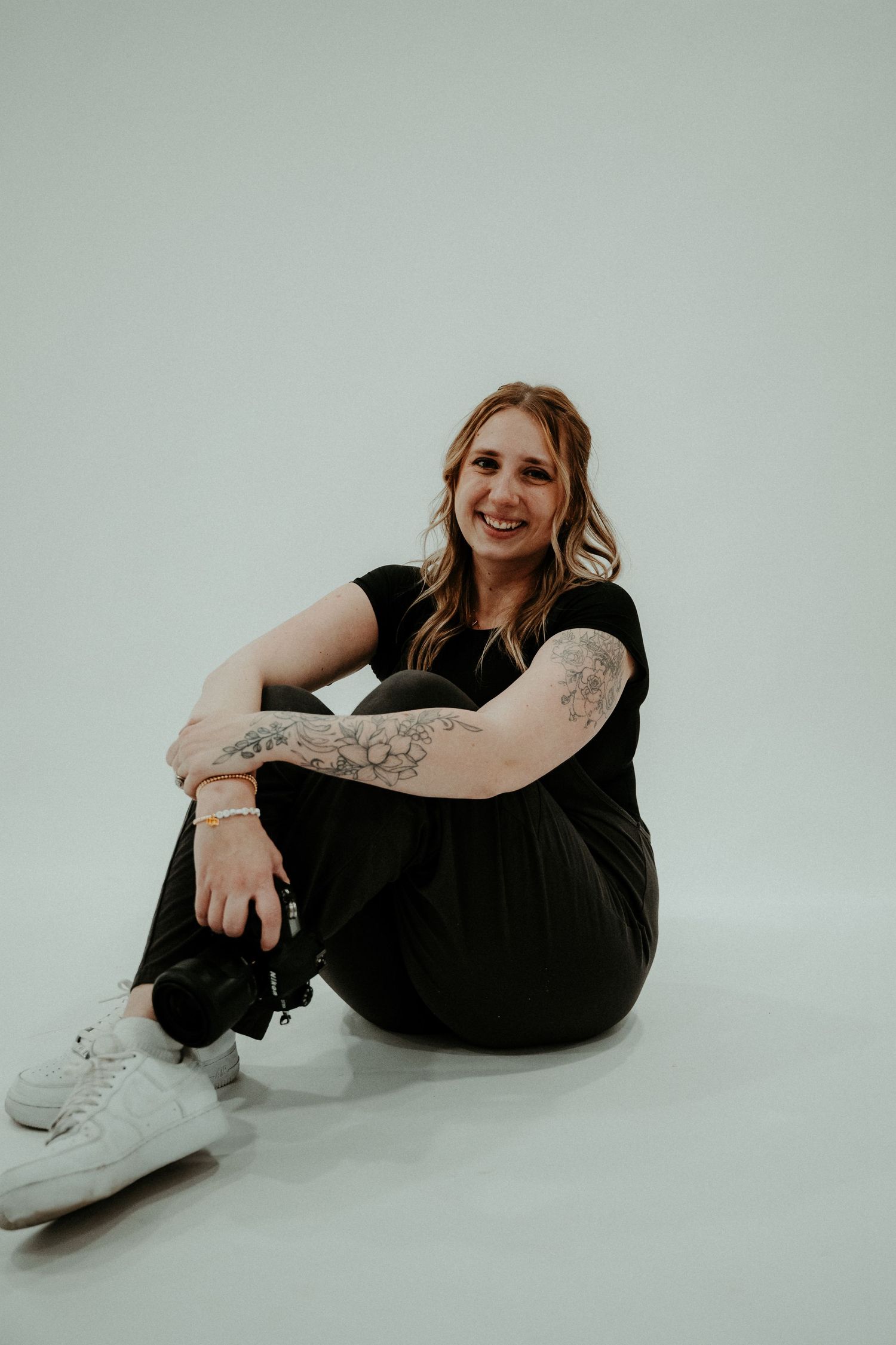 Casual portrait against white background showing tattoos and casual black outfit.