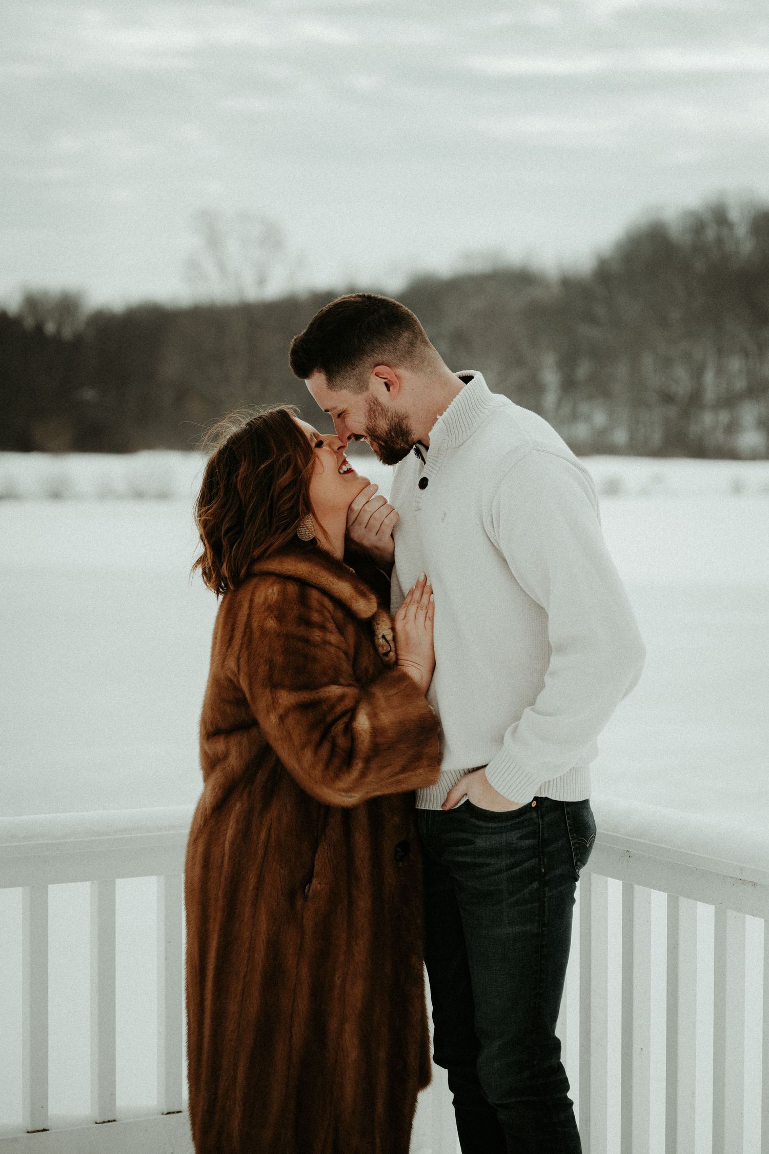 Romantic winter portrait of couple embracing on snow-covered deck.