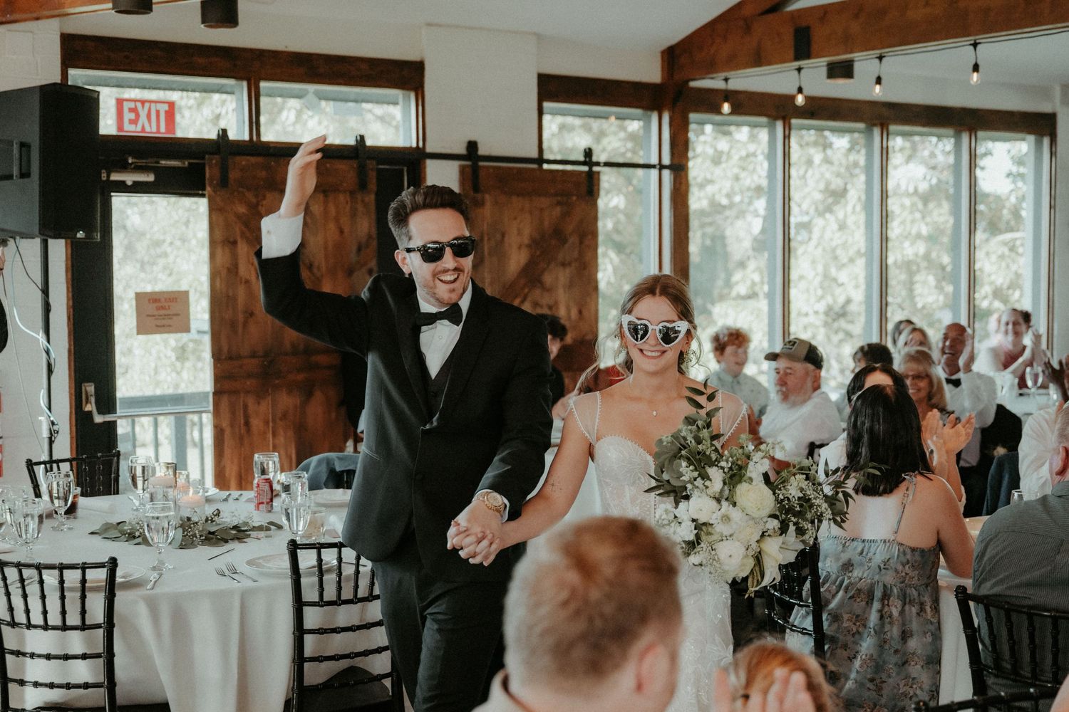 Wedding celebration in a rustic wooden venue with industrial lighting and elegant black chiavari chairs.