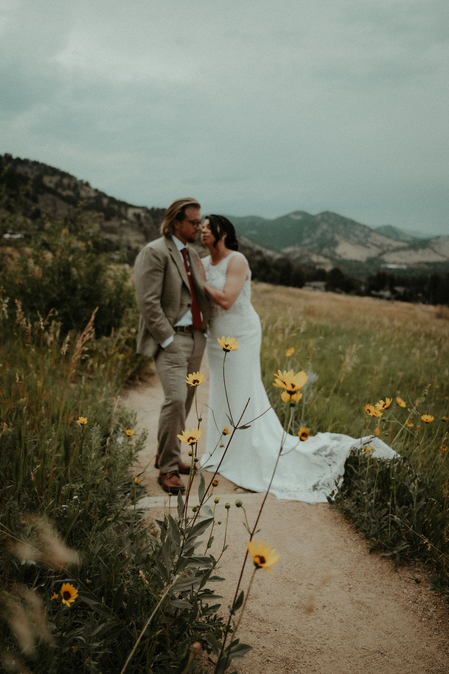 A romantic moment on a mountain trail surrounded by blooming yellow wildflowers on an overcast day. Travel Elopement Photographer