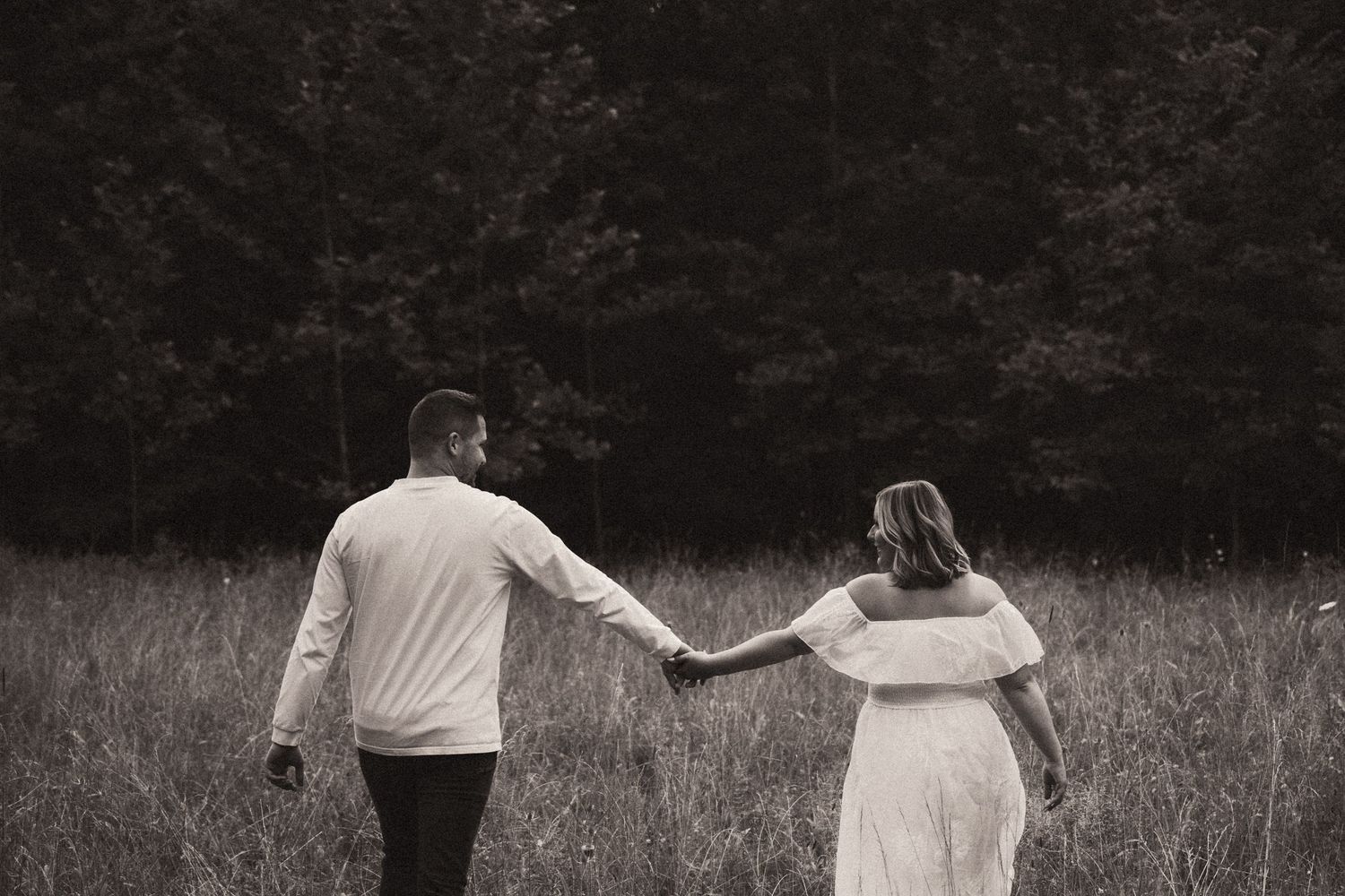 A couple holds hands while walking through a rustic field in black and white photography. Pittsburgh Wedding Photographer