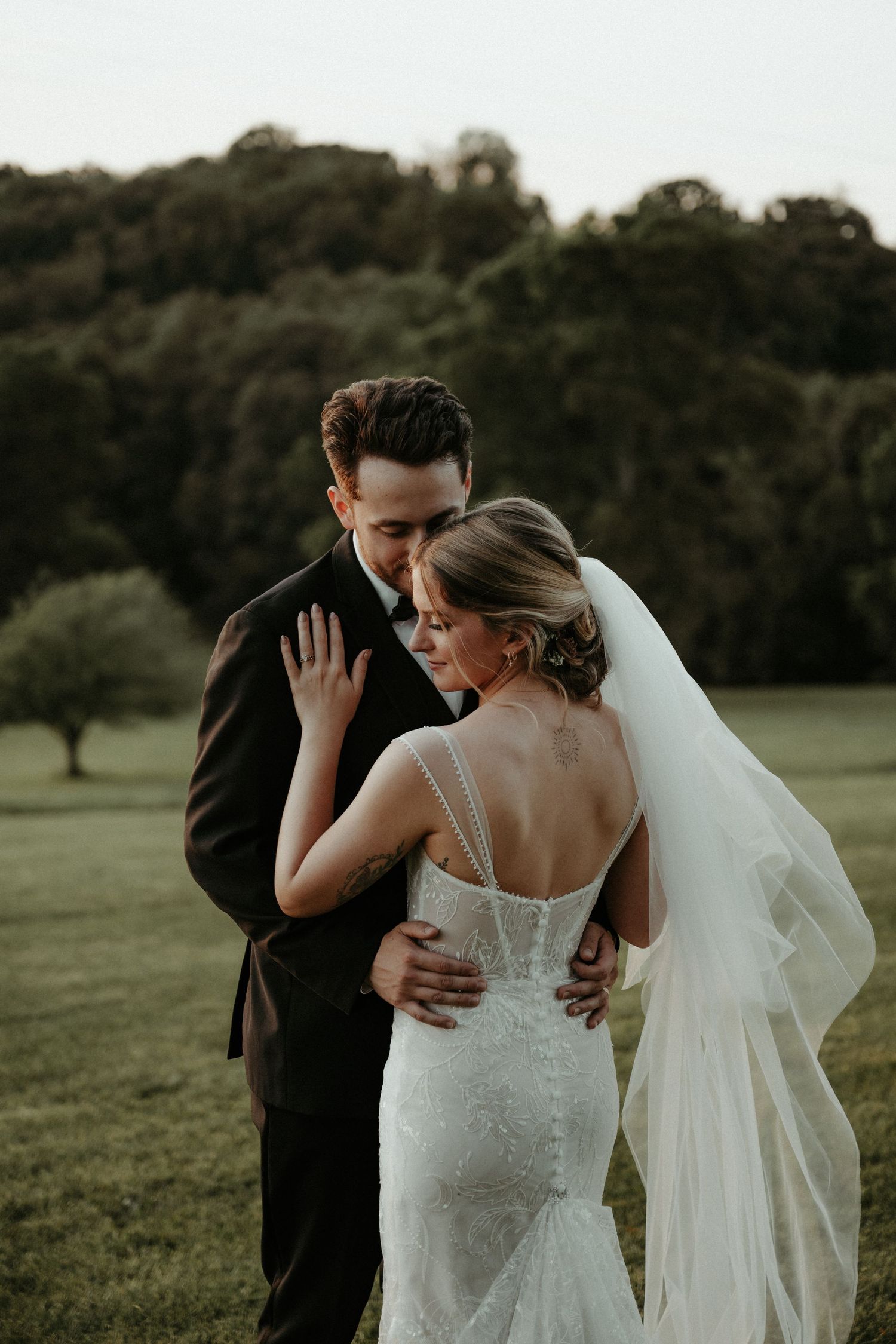 An intimate wedding moment captured outdoors with a couple in formal attire embracing in a sunlit field. Pittsburgh Wedding Photographer