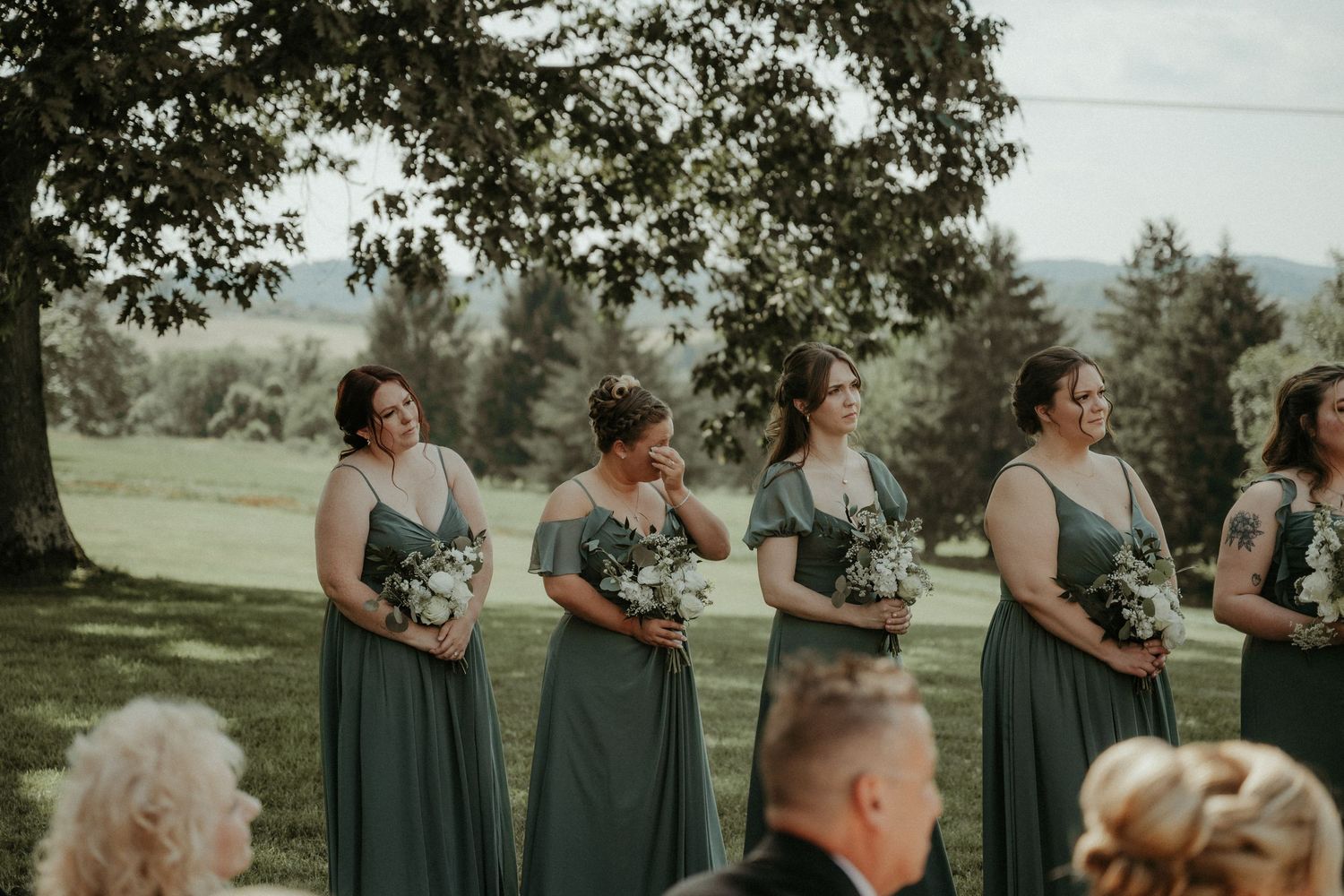 A group wearing bridesmaid dresses stands together outdoors while holding matching floral bouquets. Pittsburgh Wedding Photographer