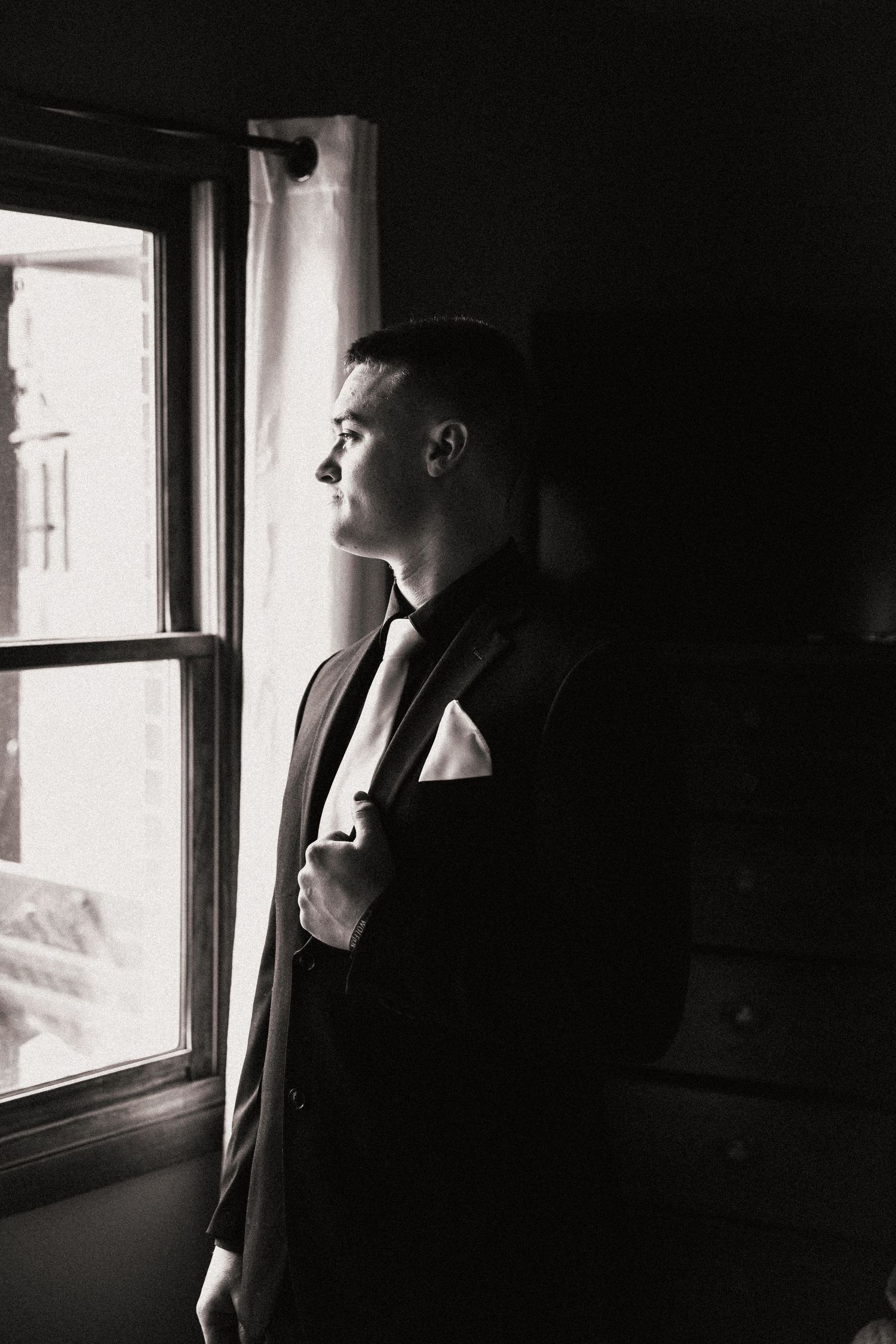 Person in formal suit gazes thoughtfully out of window in dramatic black and white portrait. Pittsburgh Wedding Photographer
