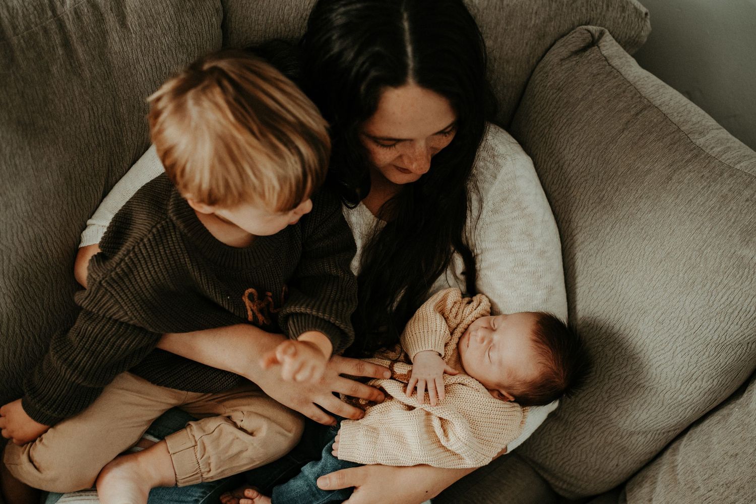 Mother and children sharing quiet moment together on gray couch.