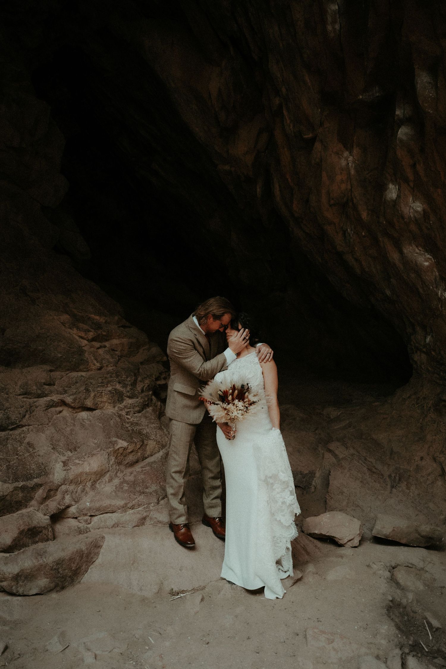 An intimate moment during their wedding photoshoot in a dramatic cave setting with soft natural lighting. Travel Elopement Photographer