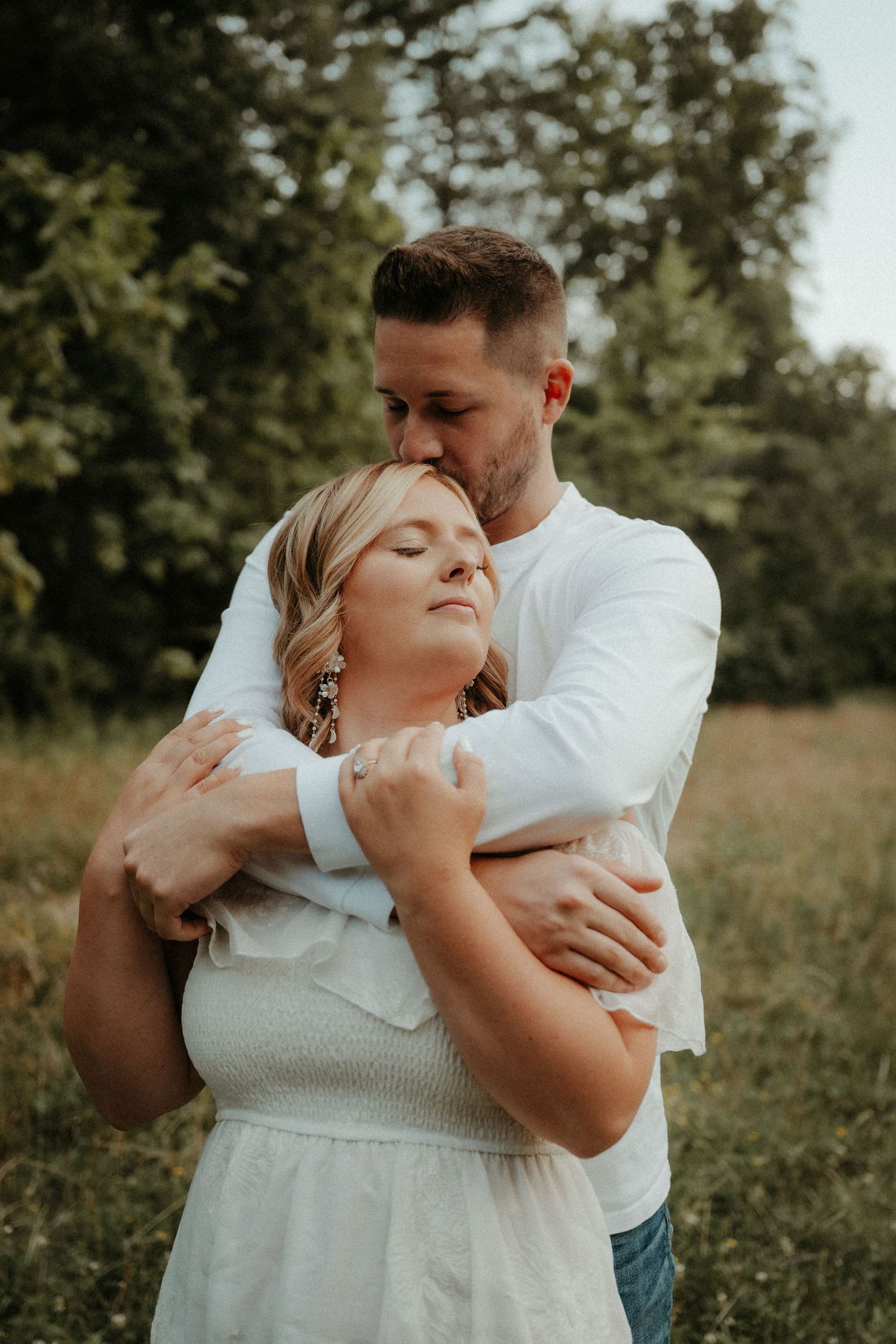 A couple embraces in a sunlit meadow wearing white and teal clothing while sharing an intimate moment. Pittsburgh Wedding Photographer