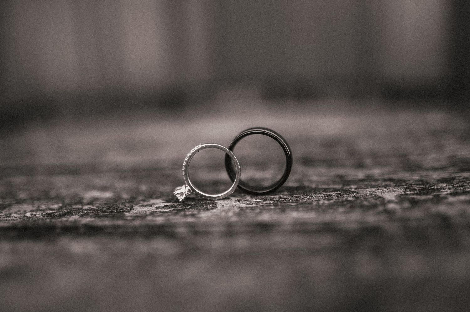 Two wedding rings photographed in dramatic black and white on a textured surface.