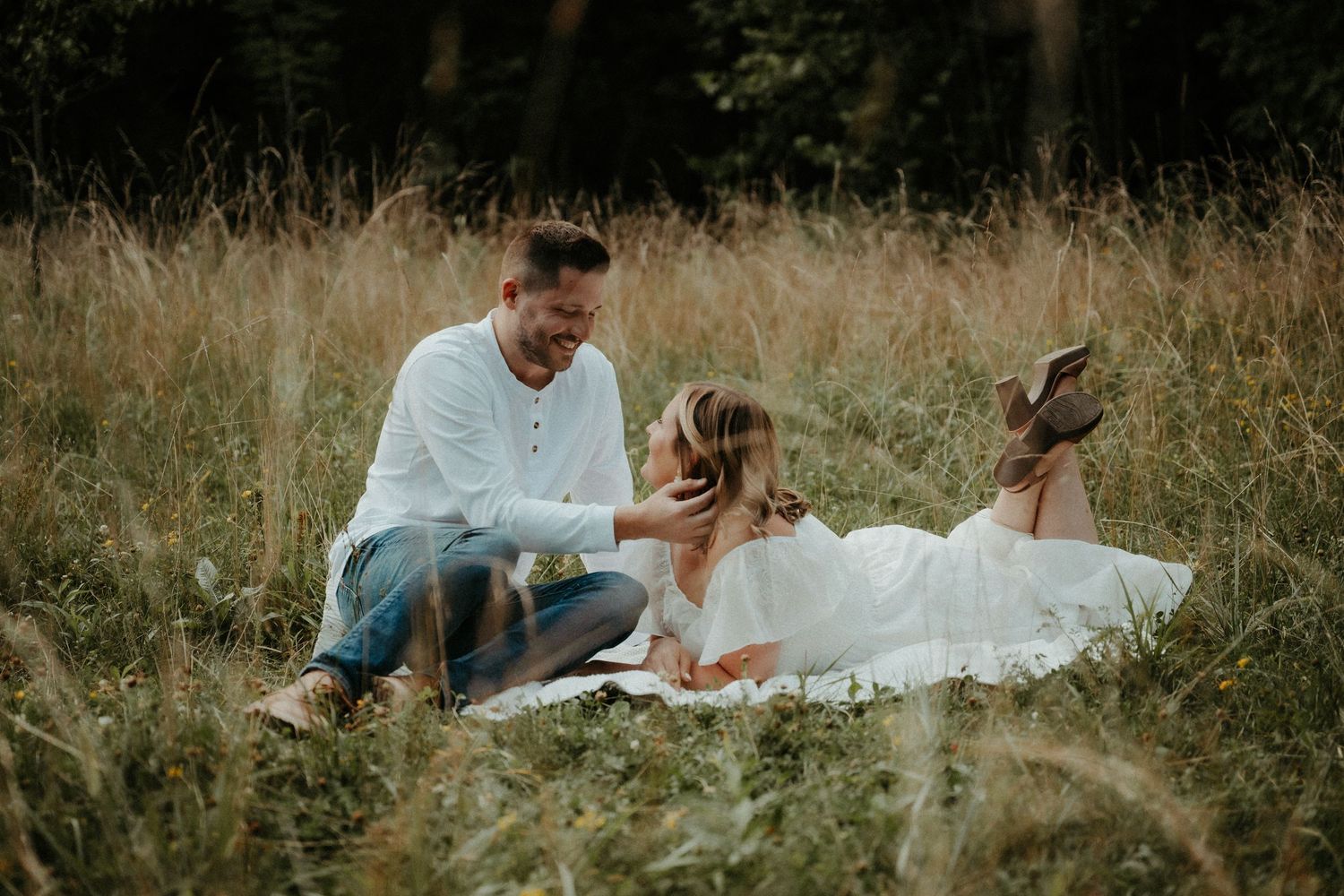 People sitting together in a tall grassy field on a sunny day, surrounded by natural meadow vegetation. Pittsburgh Wedding Photographer
